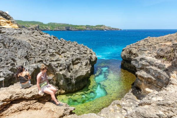 Nusa Penida, Indonesia - September 16, 2018: Unidentified woman sitting at the edge of cliff at Angel's Billabong, a natural ocean-side infinity pool in Nusa Penida Island, Bali, Indonesia.
